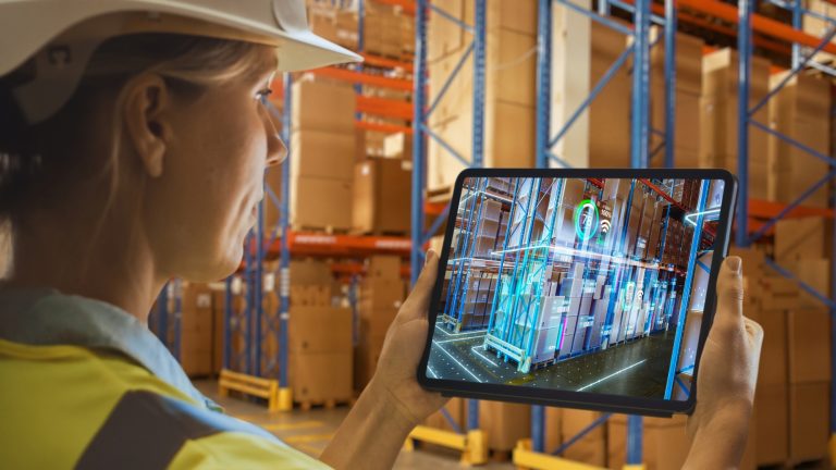 Un travailleur en casque de sécurité tient une tablette dans un entrepôt.